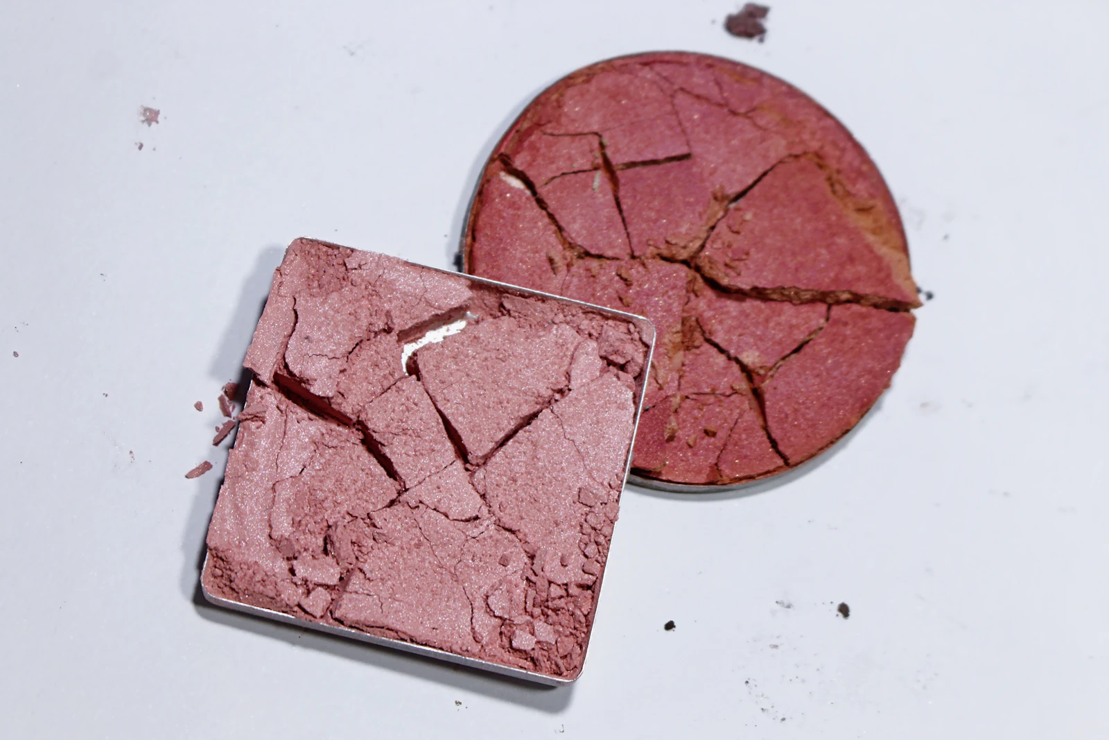 Two cracked pans of pressed rose powder on a white surface