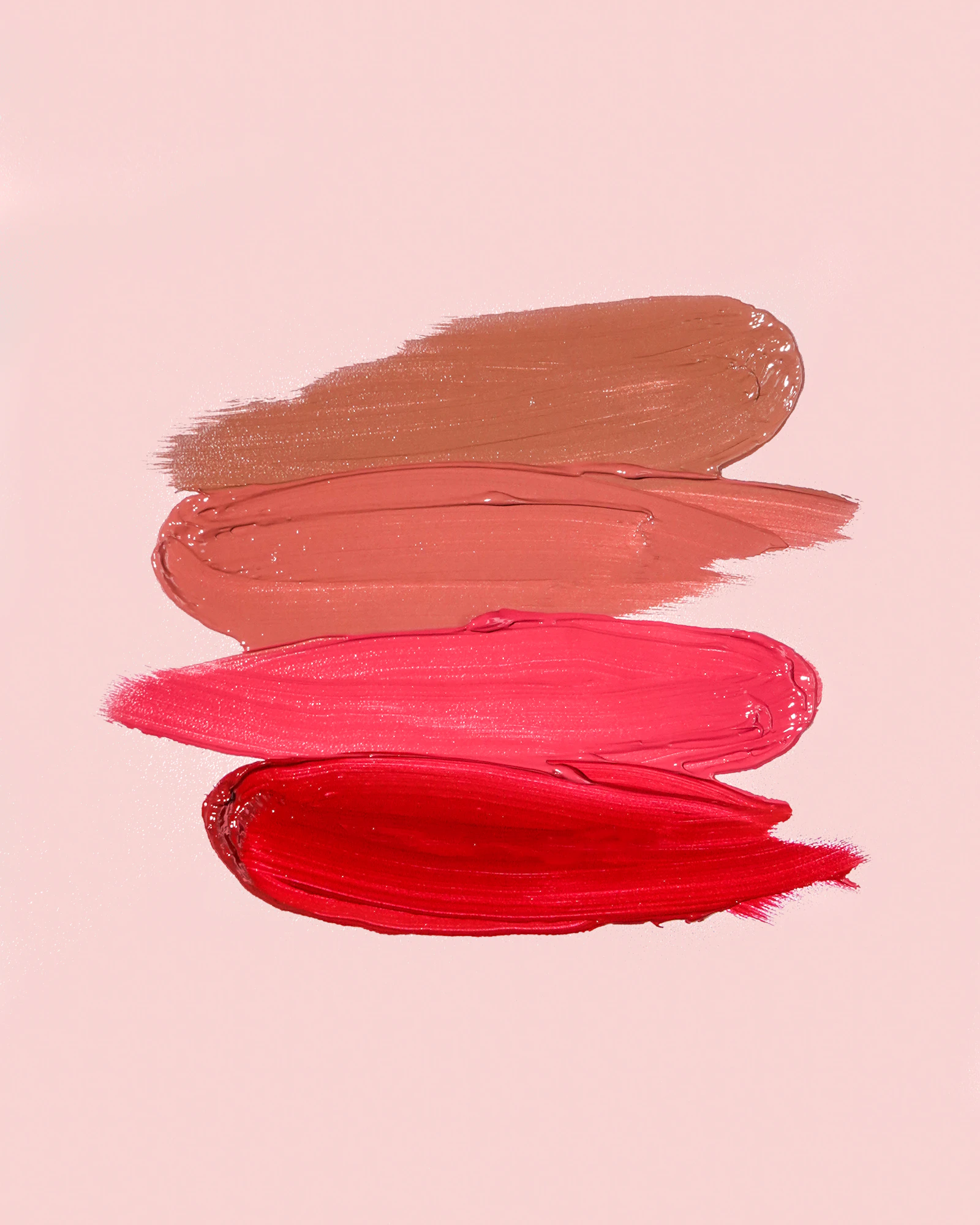 Four smears of lip color, from brown and peach to pink and red, on a pink background