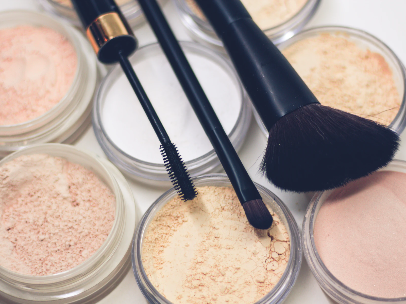 Open jars of loose powder in pale skin tones with a powder brush and a mascara wand