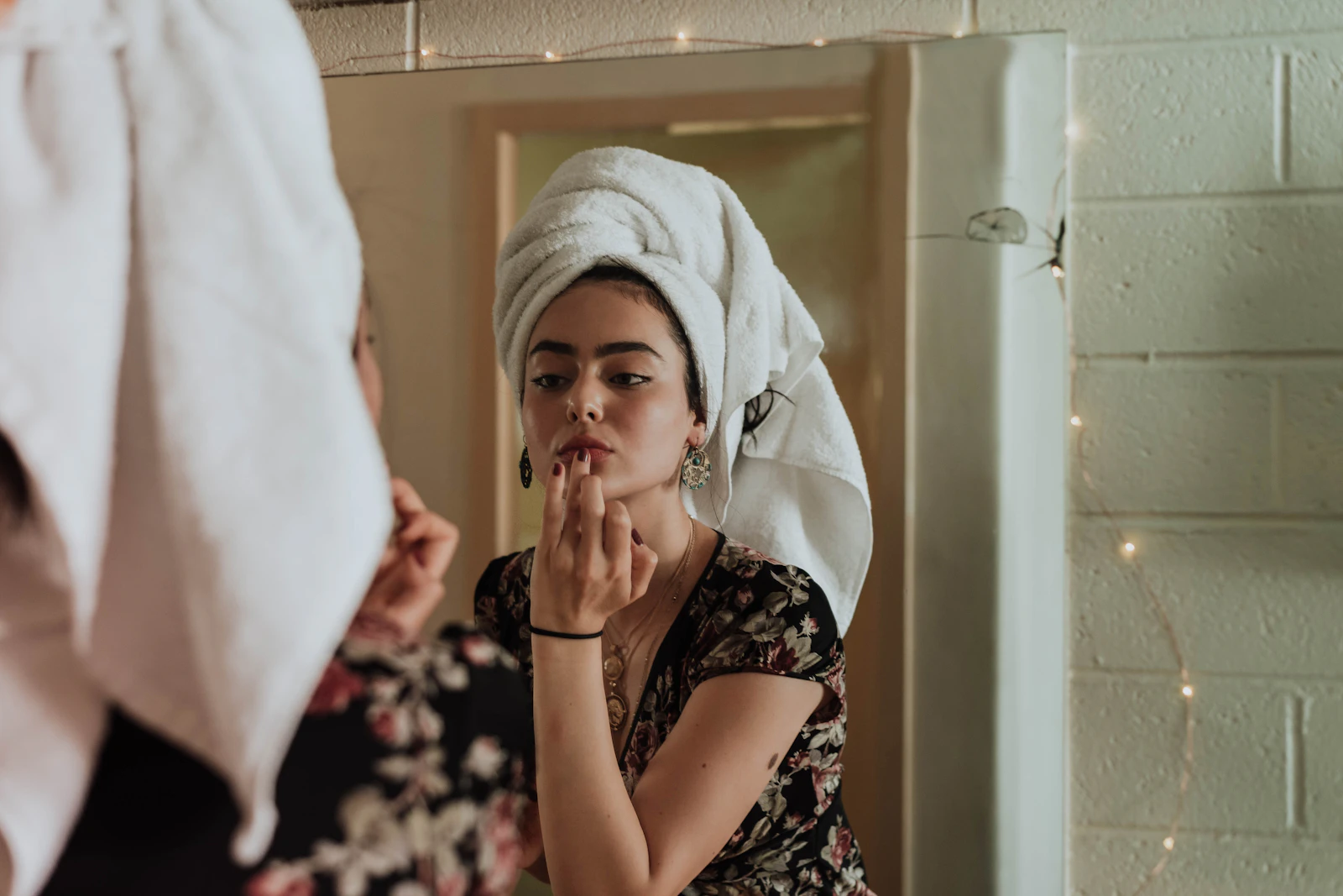 Woman with her hair in a towel applying lip color at a bathroom mirror